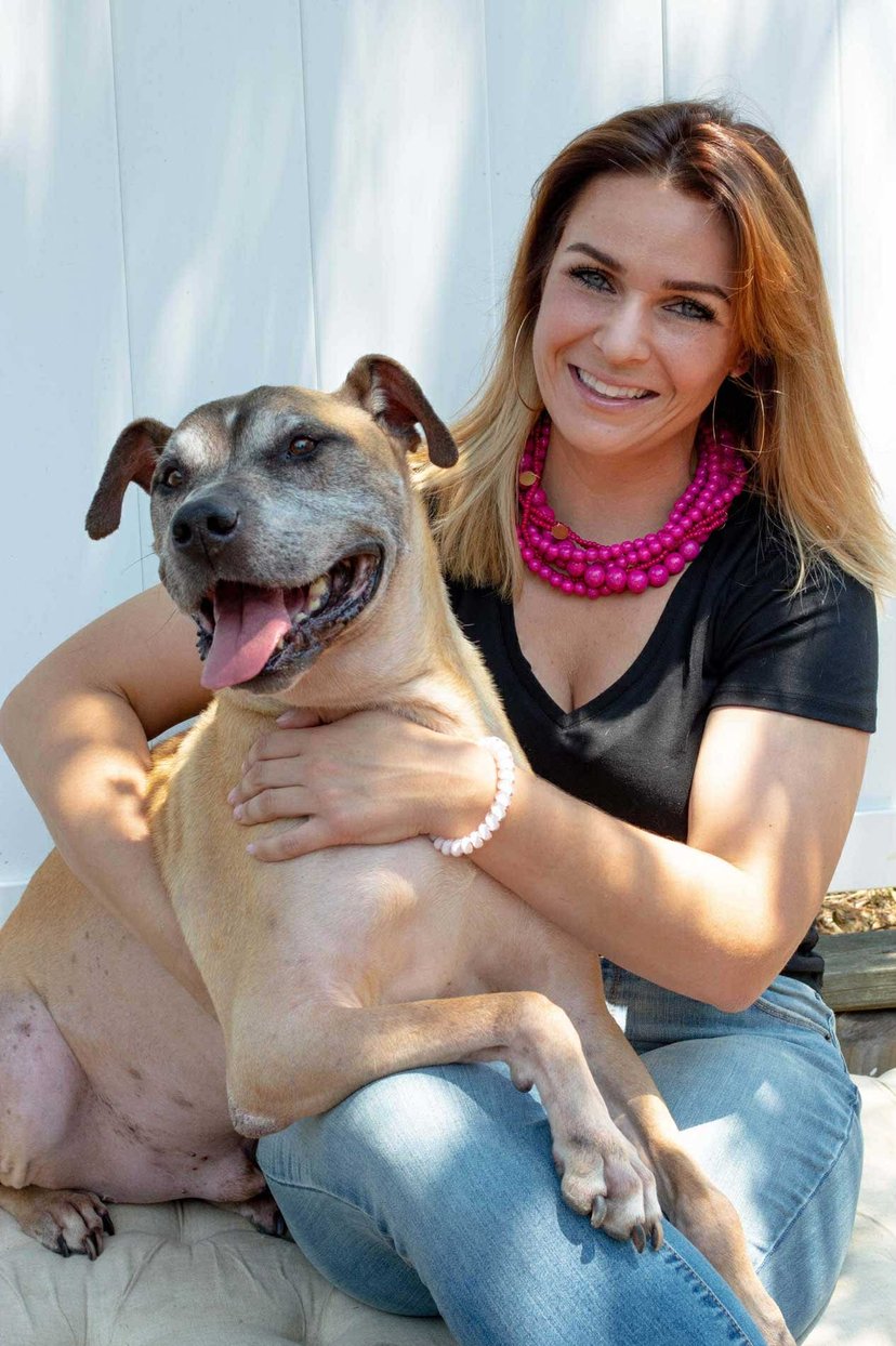 Paulina Beck of The Mannered Mutt smiling and hugging a tan dog in Conroe, TX